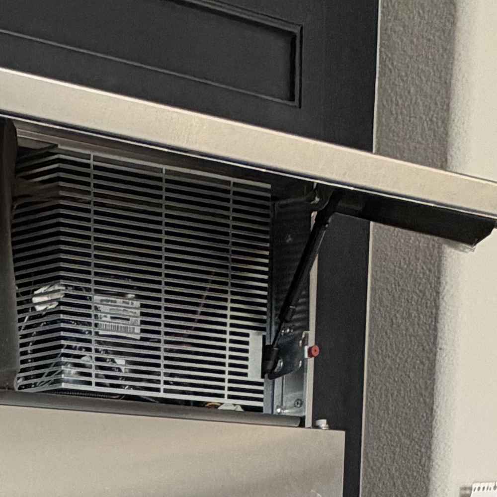 Condenser and fan behind the open service grille of a built-in refrigerator during a Spark repair in San Diego