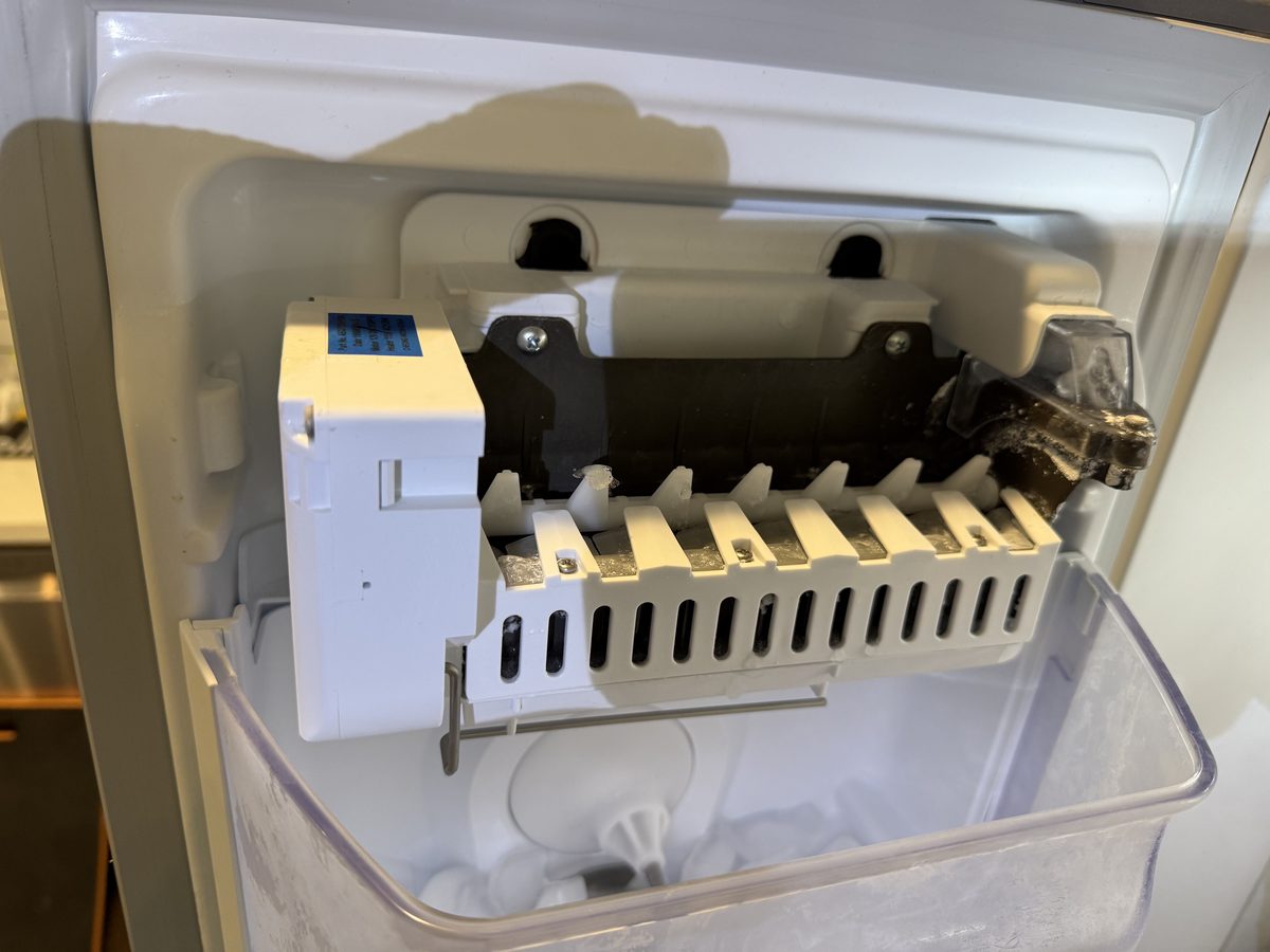 Rake-style refrigerator ice maker assembly mounted above its ice bin during a Spark service call in San Diego