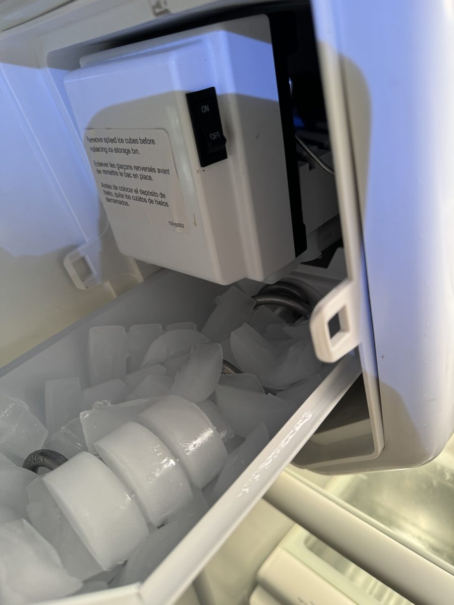 Refrigerator ice maker with its on/off switch next to a bin full of crescent ice cubes during a Spark service call