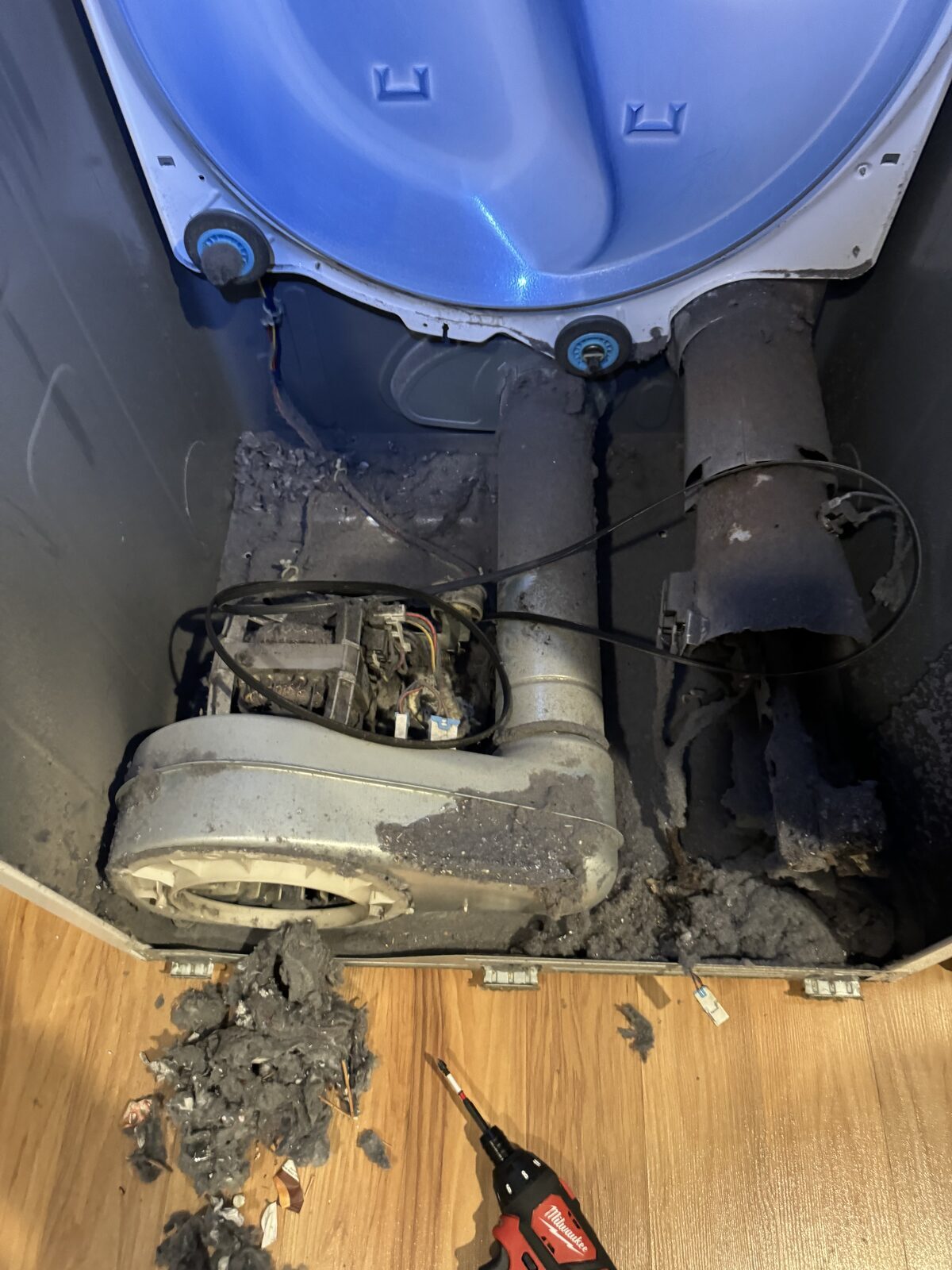 Dryer with the front panel removed showing a blower housing and exhaust duct packed with lint