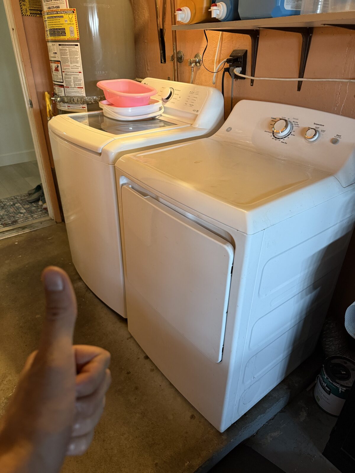 Top-load washer next to a GE dryer in a garage laundry corner beside the water heater