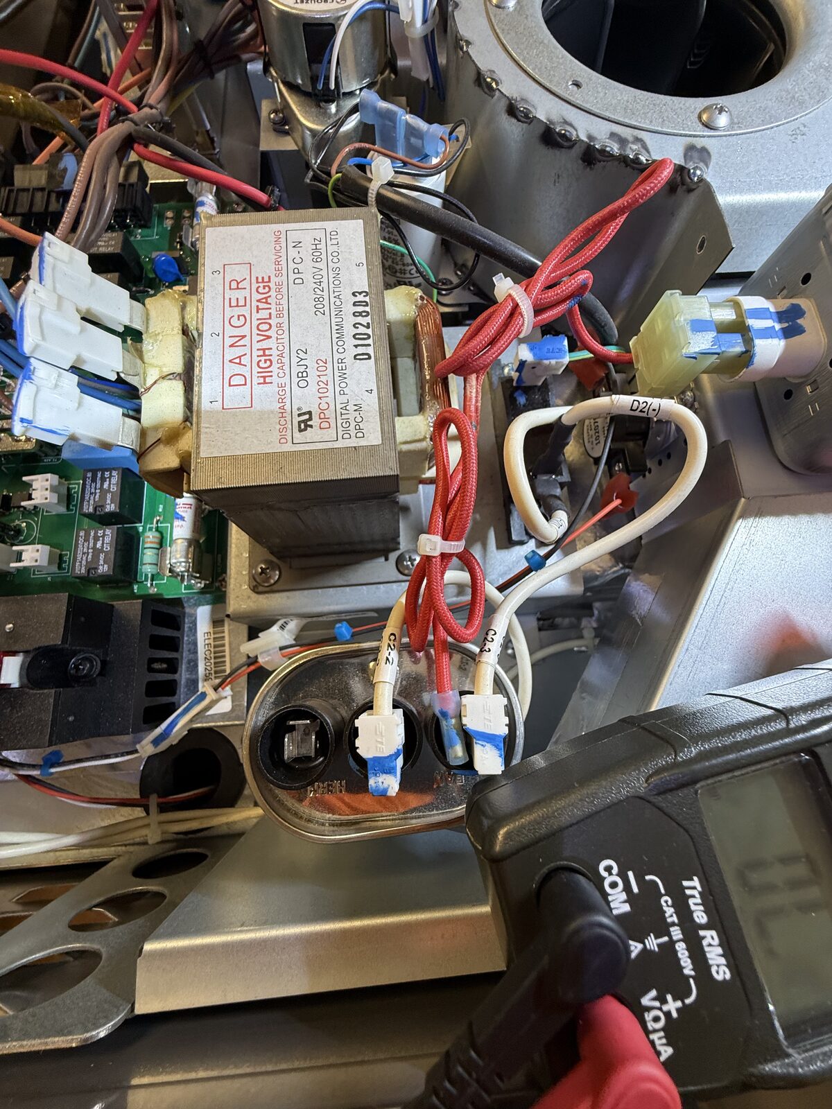 Microwave section of a combination wall oven opened for testing: relay board, high-voltage transformer and capacitor, meter in hand