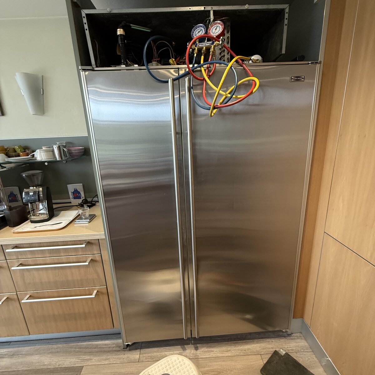 Built-in stainless side-by-side refrigerator with the top grille off and manifold gauge hoses hanging over the doors during a Spark sealed-system check