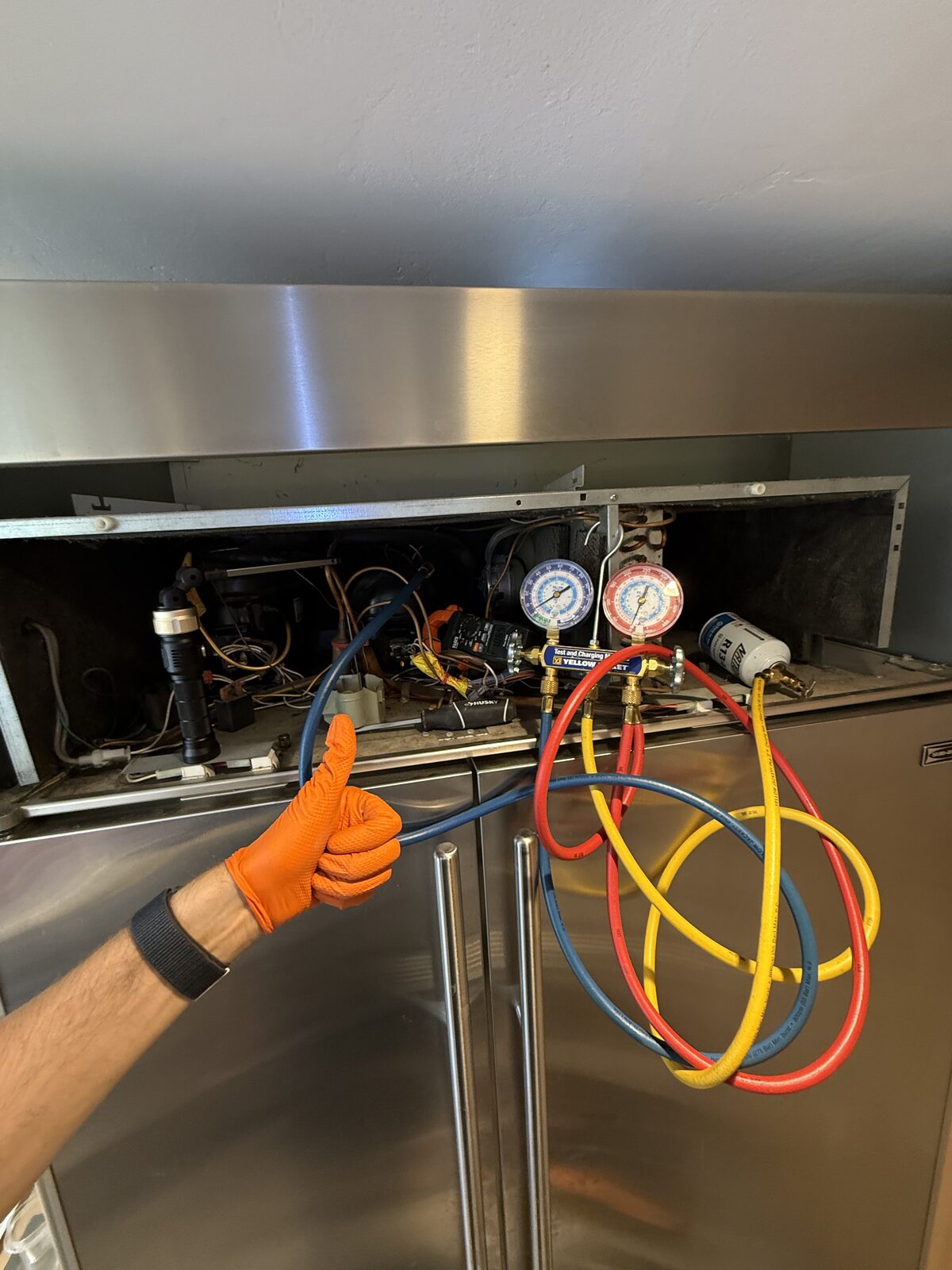 Manifold gauges connected to the top compressor compartment of a built-in refrigerator during a Spark sealed-system check