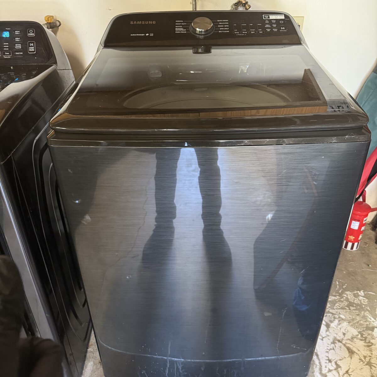 Black Samsung top-load washer with a glass lid in a garage laundry on a Spark Appliance Repair service call