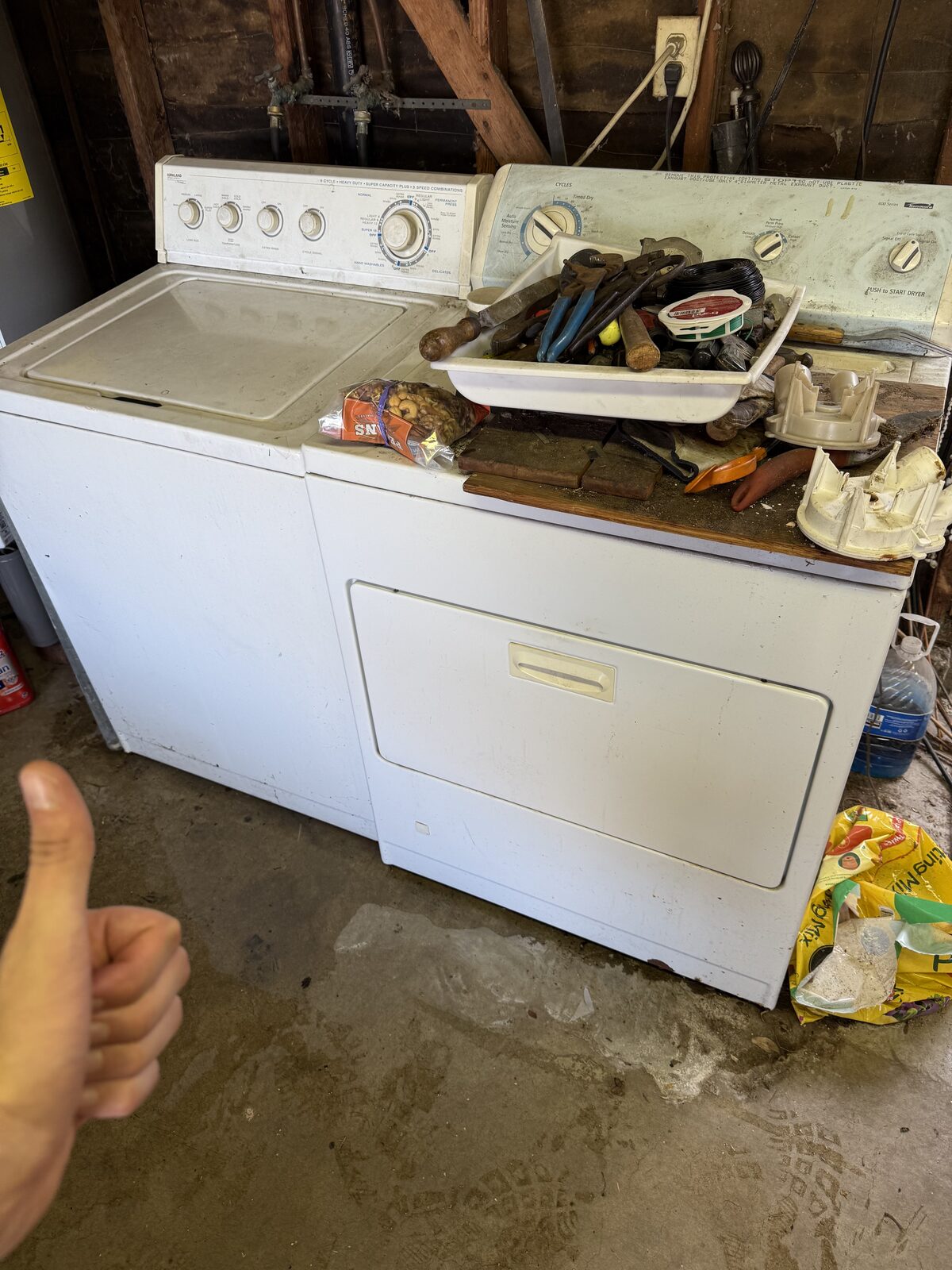 Top-load washer in a garage with removed agitator parts and hand tools laid out on the dryer during a Spark repair