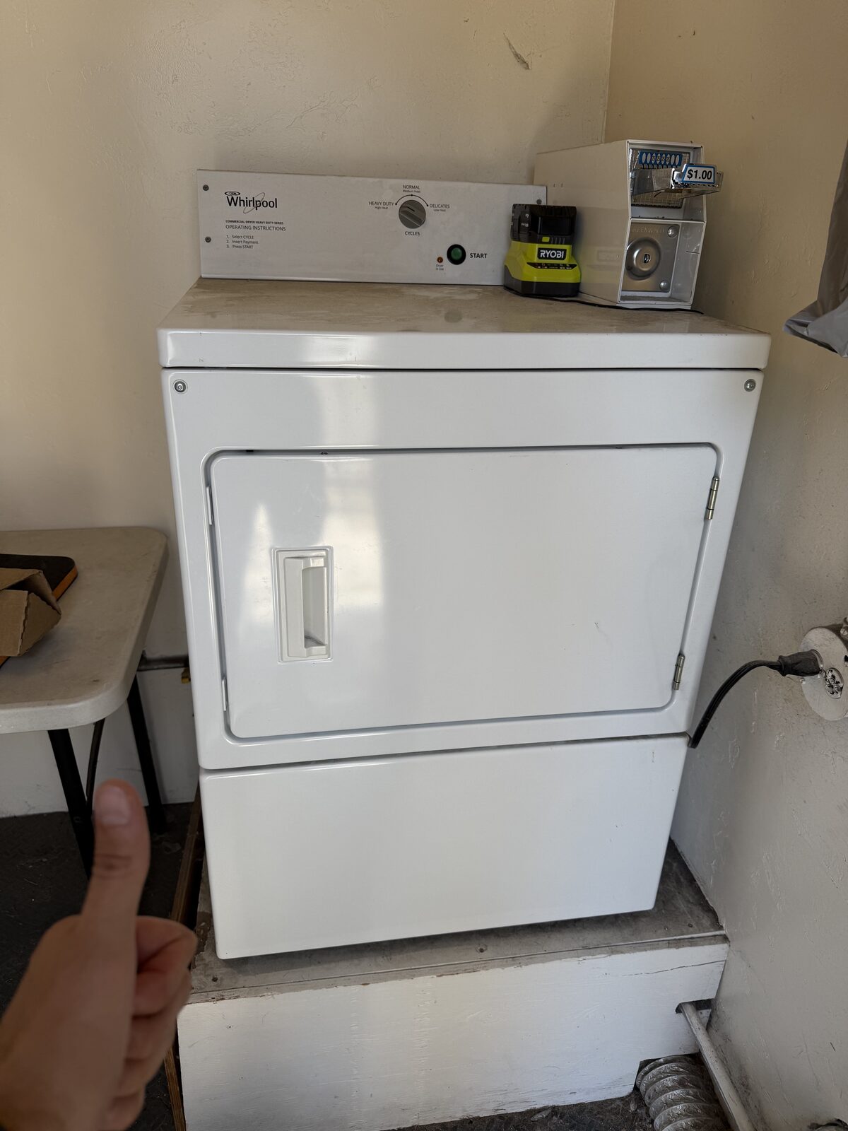White coin-operated Whirlpool commercial dryer on a raised platform in a shared laundry room