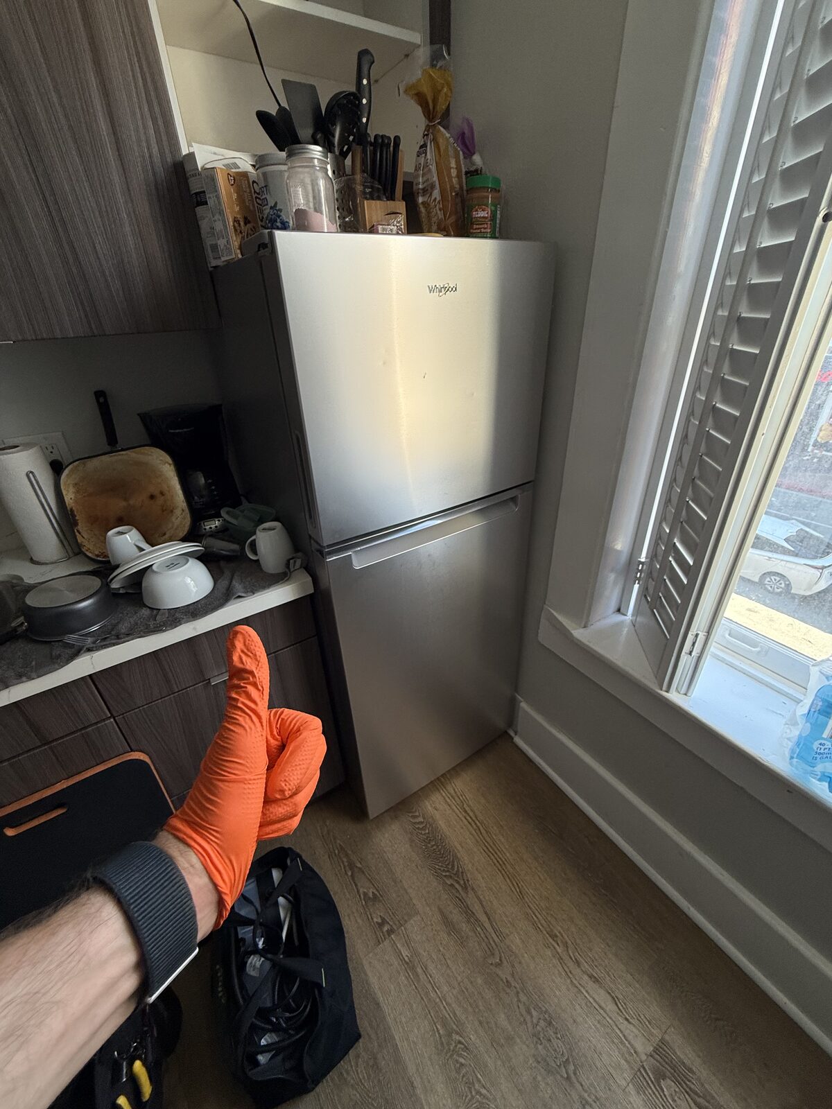 Compact stainless Whirlpool top-freezer refrigerator in a kitchen with a Spark technician’s gloved hand in front